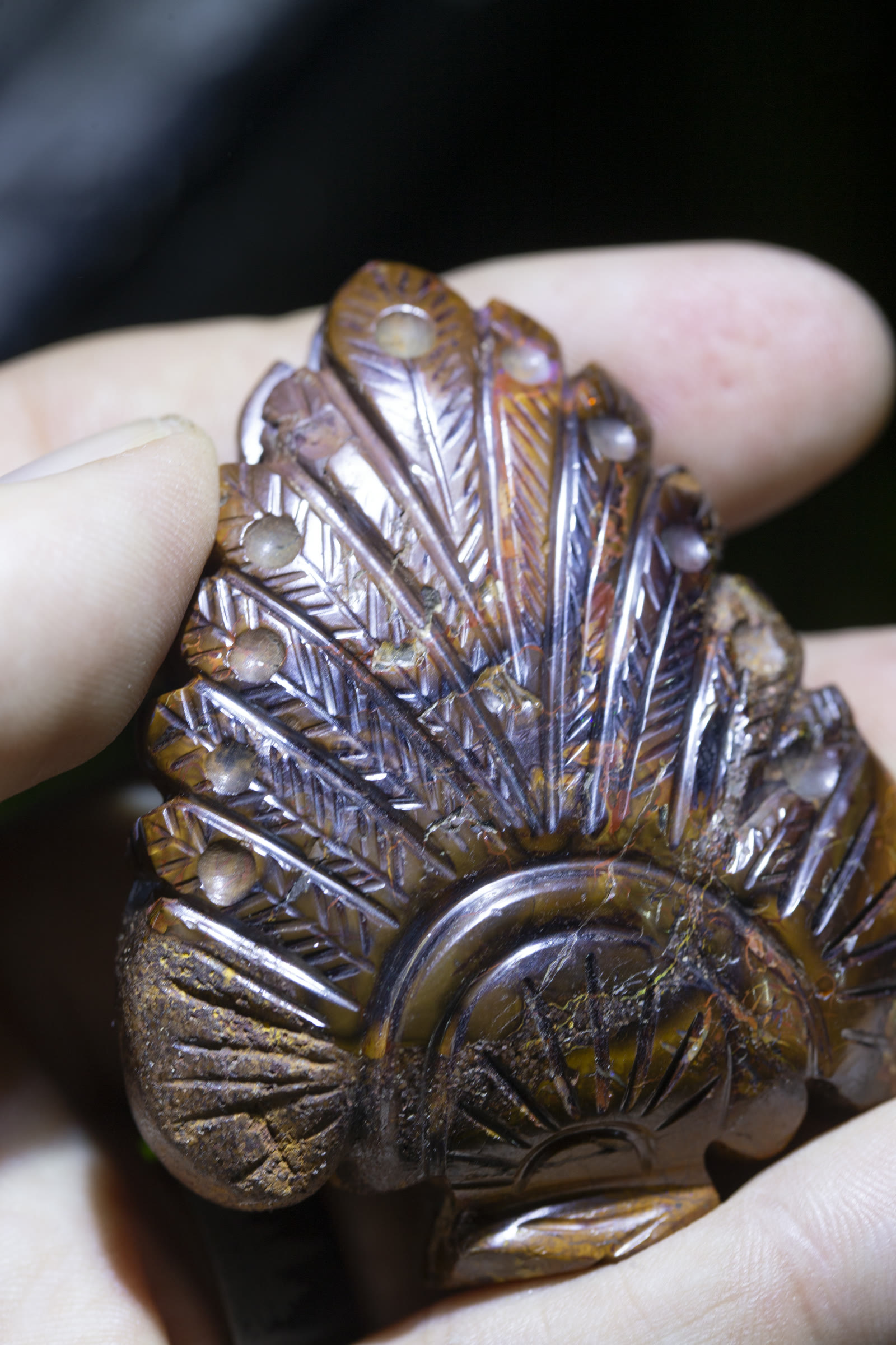 A carved Native American headdress in boulder opal — intricate feather and bead detail in dark ironstone matrix with opal color peeking through.