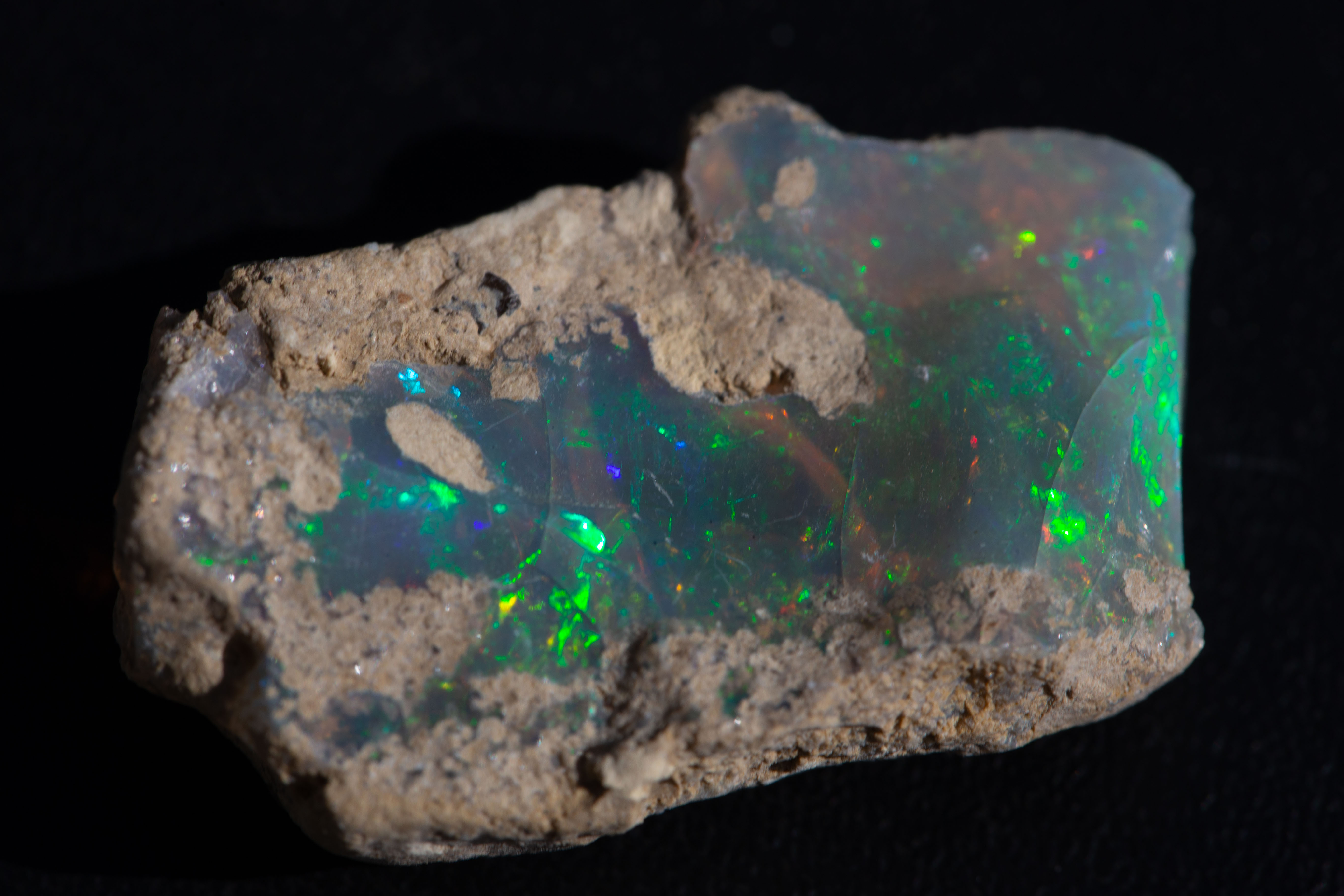 Rough Ethiopian Welo opal on sandy matrix, green and blue fire visible through the translucent body.