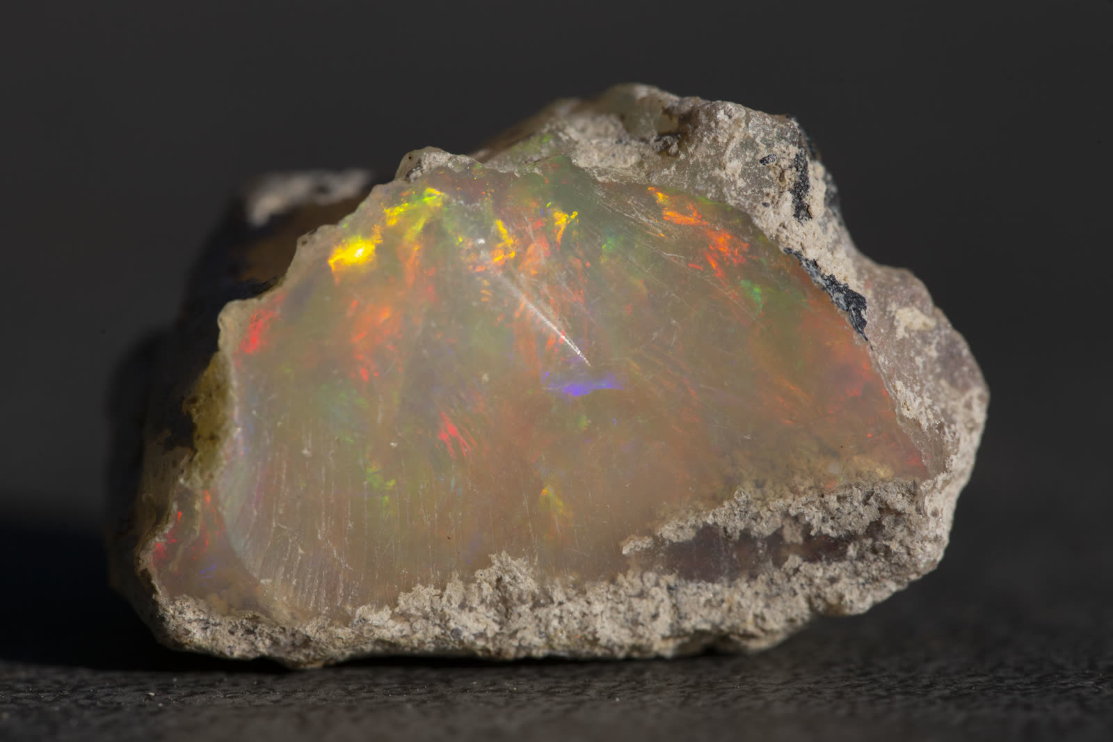 Large rough Ethiopian Welo opal with vivid red, orange, and yellow play-of-color across a milky cream body, sandy matrix at edges.